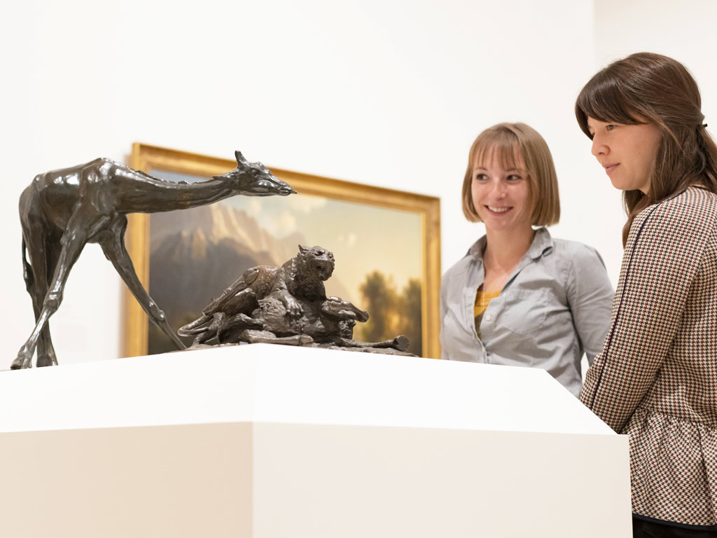 Two women are looking at small bronze sculptures of animals.